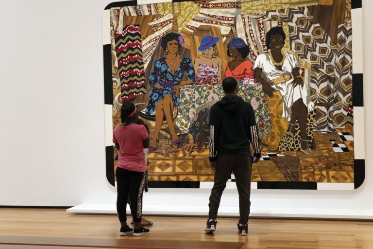 Photo of two people looking at a bright colored painting of three women. 